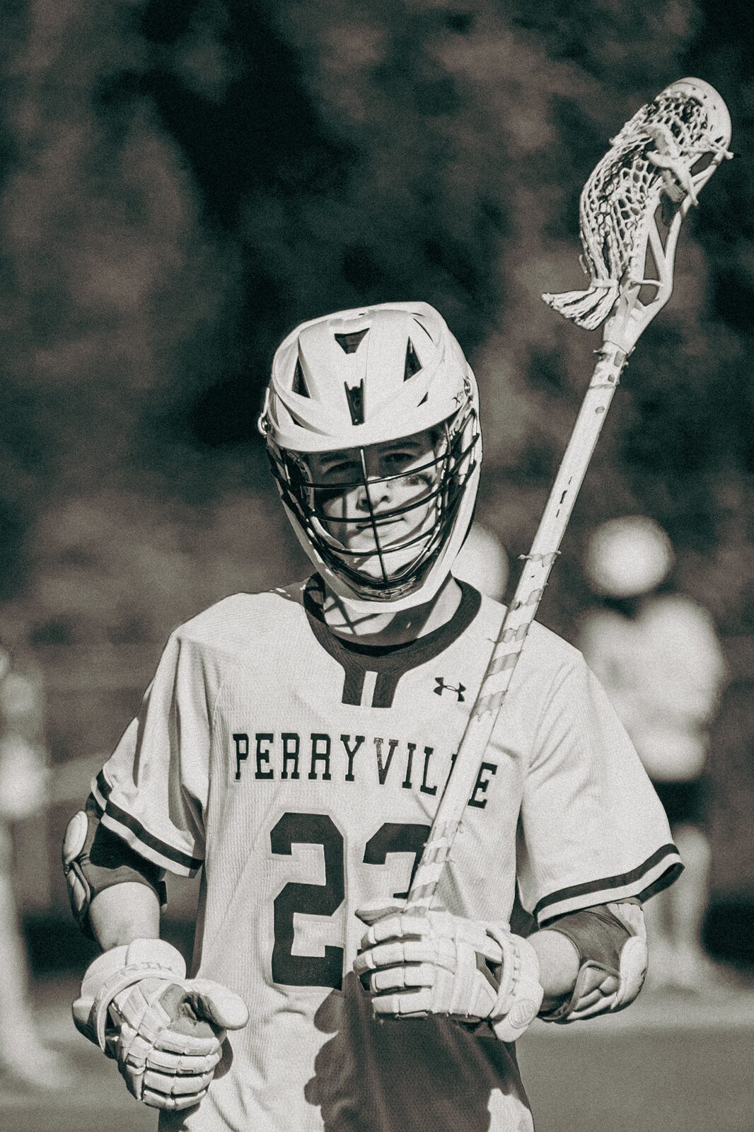 Black and white photo of a lacrosse player walking off with his stick raised and blossoming trees behind him