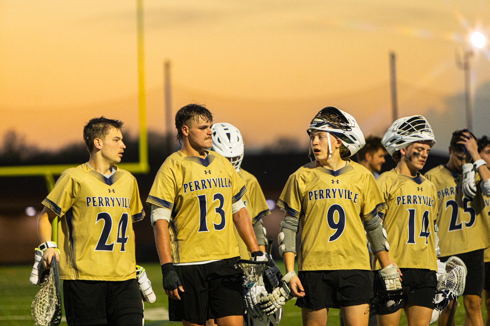 Lacrosse team walking off the field together in gold jerseys under a peach and orange sunset