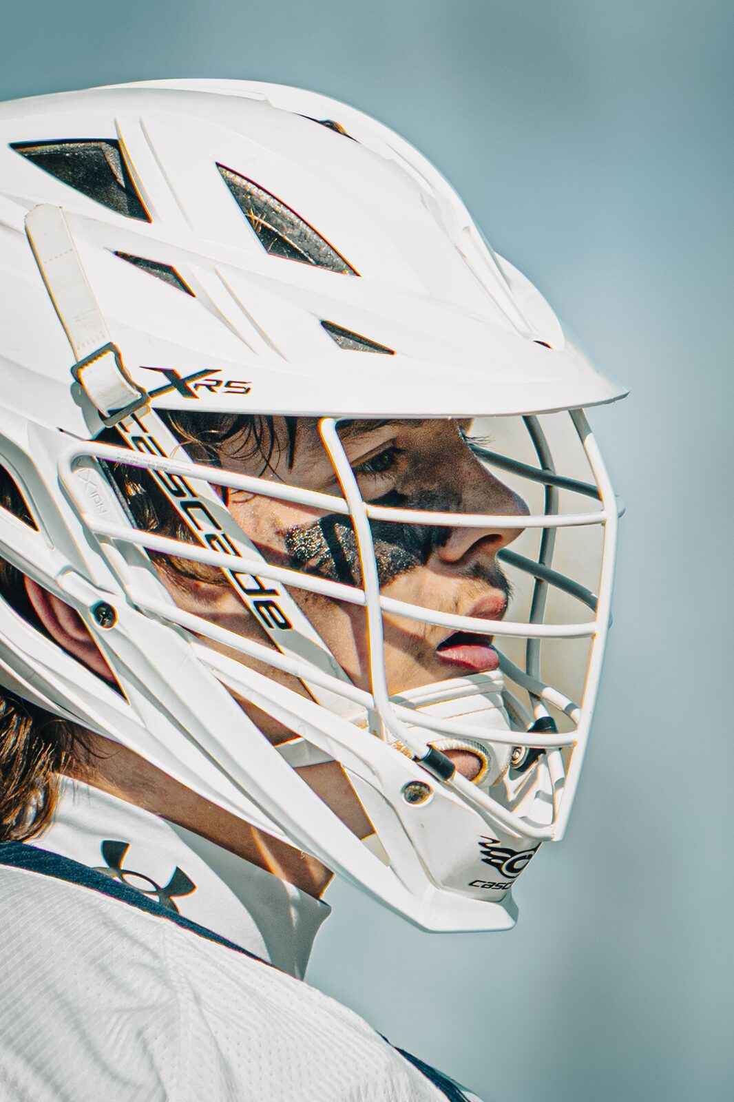 Tight portrait of a lacrosse player's face framed inside his white helmet cage